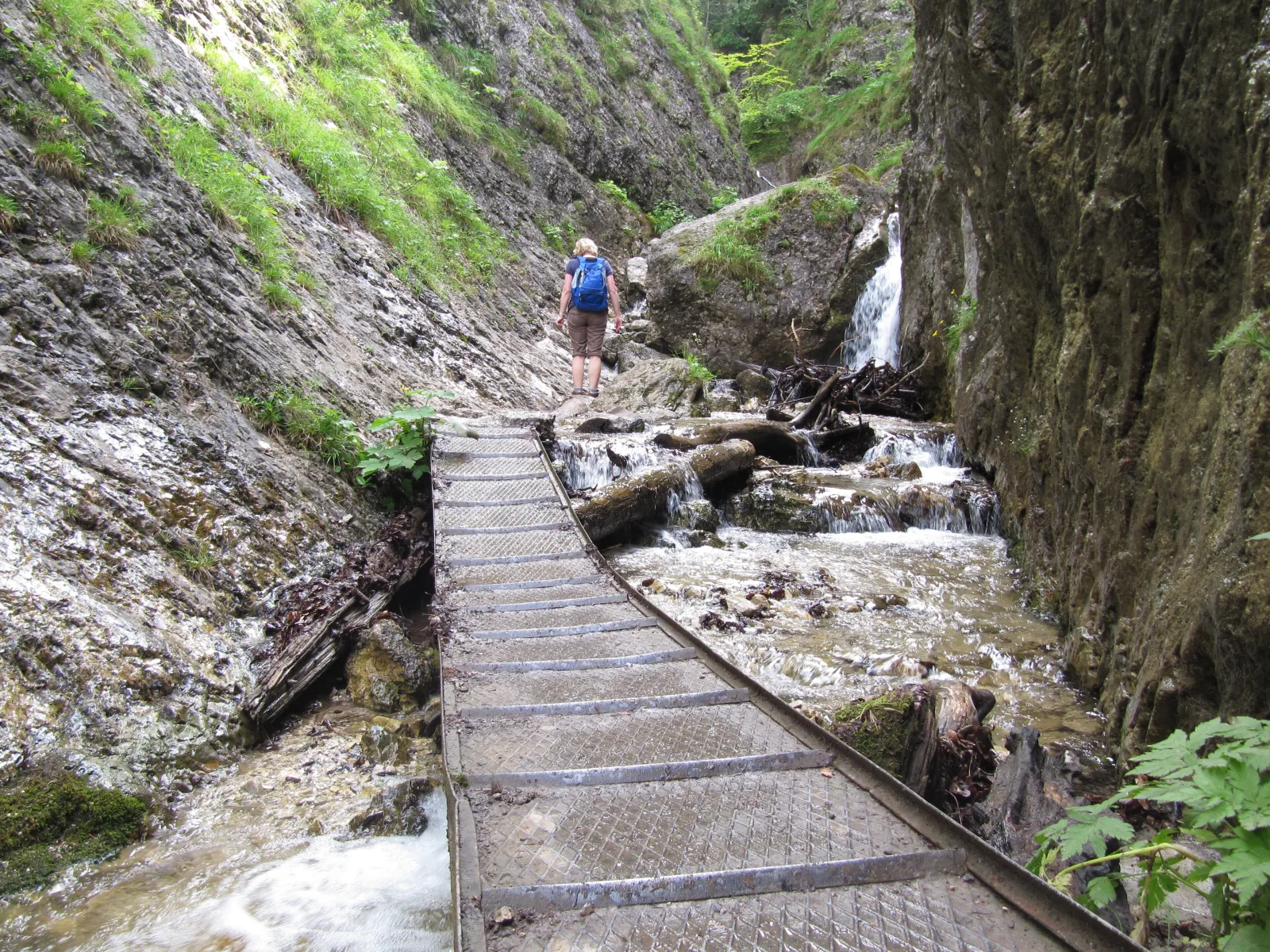 Kovová lávka popri potoku a vodopáde v skalnej tiesňave Horných dier, turistka s batohom