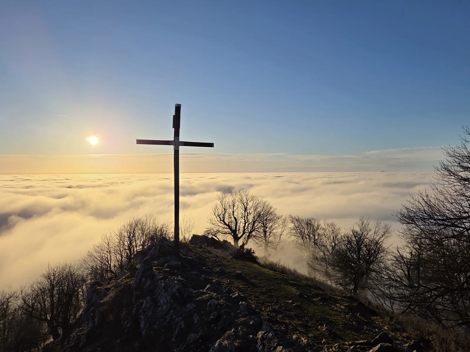 Drevený kríž na skalnatom vrchole Vysokej v Malých Karpatoch nad morom hmly v zimnom popoludní