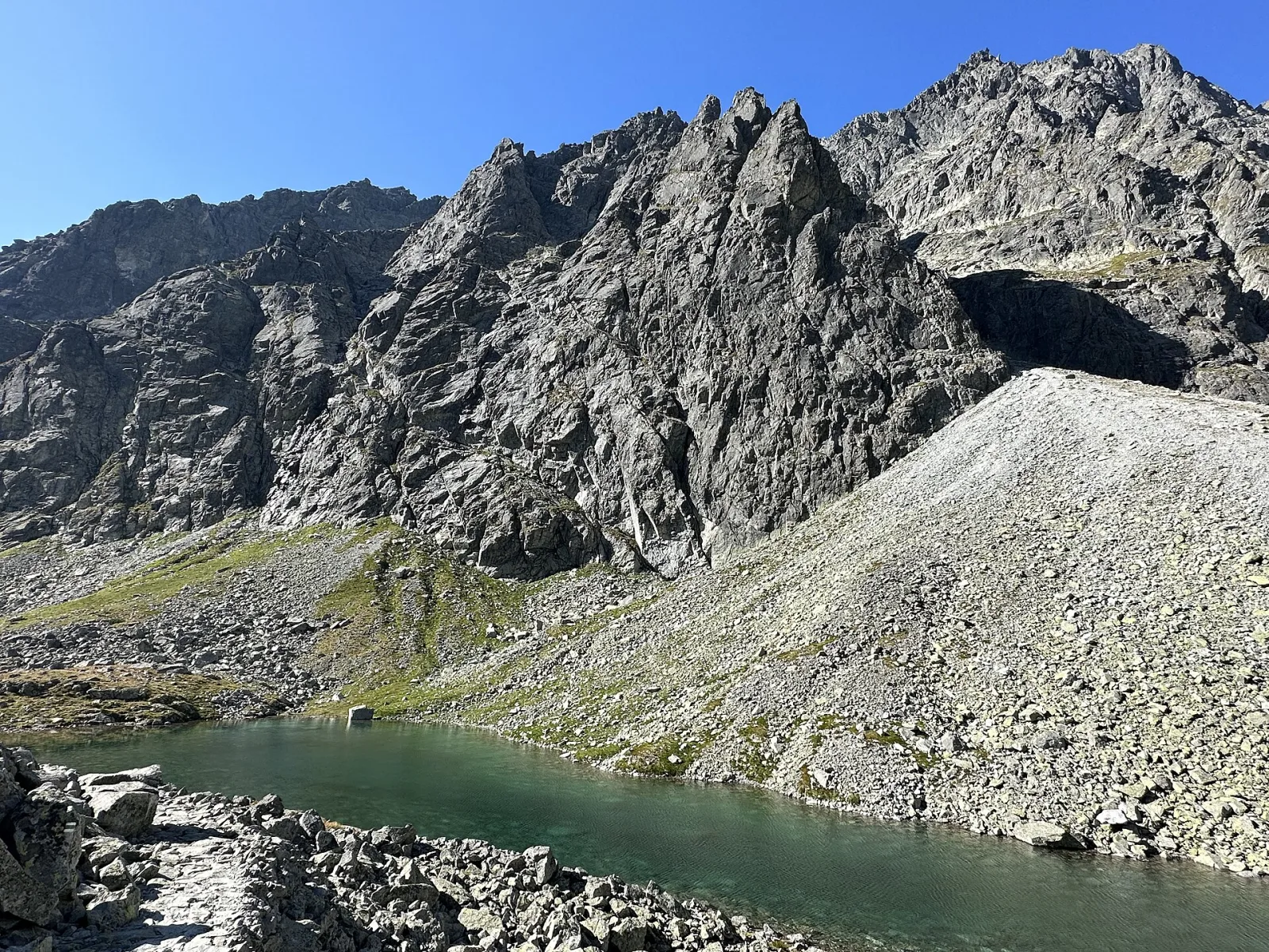 Dlhé pleso vo Velickej doline pod skalnými stenami Gerlachovského masívu, so sutinovým svahom nad hladinou