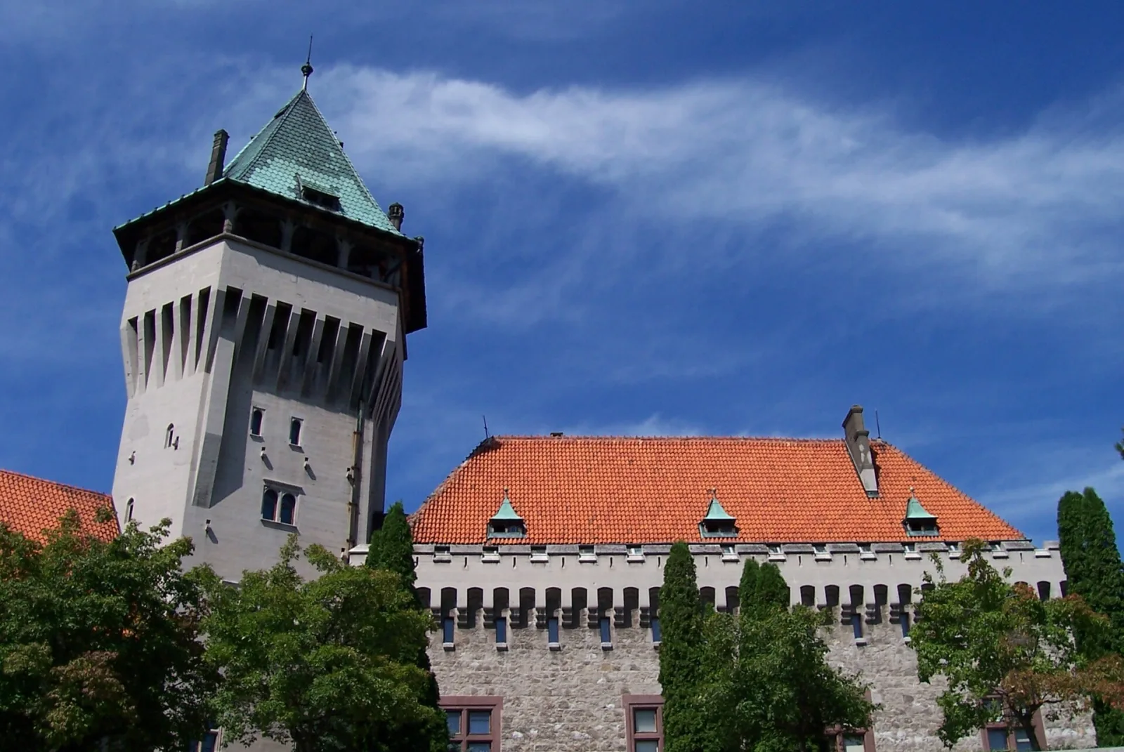 Vysoká veža Smolenického zámku s červenými strechami a hradbami na pozadí modrej oblohy